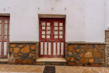Gaucin, İspanya - 27 Ocak 2025 - İspanya 'nın Gaucin şehrinde geleneksel bir caddede, taş duvar tabanı ve beyazlatılmış cephe ile çevrili kırmızı ve beyaz panelli Rustik ahşap kapı.