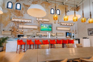 Sotogrande, İspanya - 27 Ocak 2025 - Mermer tezgahlı golf kulübü barı, kırmızı sandalyeler, kolye ışıkları, golfü gösteren TV ve şık ve davetkar iç dekorasyonlu duvarlar.