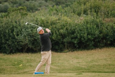Bir golfçü, golf oynarken yemyeşil bir golf sahasında, yemyeşil bitki örtüsüyle çevrili bir salıncakta sallandıktan sonra tamamlar..