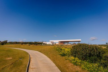 Endülüs, İspanya, 30 Ocak 2025 La Hacienda golf sahasında açık mavi bir gökyüzünün altında yeşil ve sarı çiçeklerle çevrili kıvrımlı bir patikası olan modern bir kulüp evi..