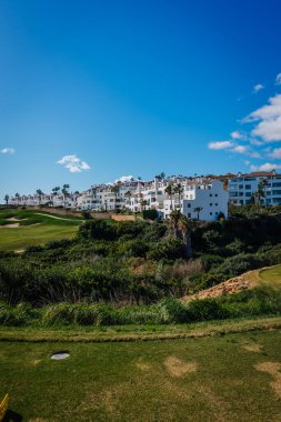 Endülüs, İspanya, 30 Ocak 2025 La Hacienda golf sahasının canlı yeşillikleri, tepedeki beyaz modern binalar, palmiye ağaçları ve açık mavi gökyüzü..