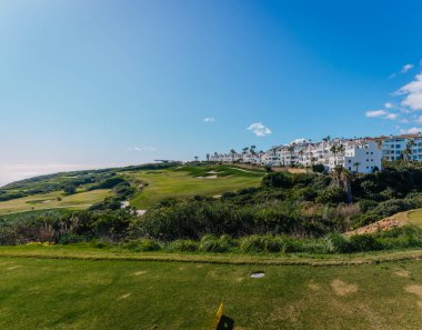 Endülüs, İspanya, 30 Ocak 2025 - Bereketli otlaklar, modern beyaz binalar ve parlak güneşin altında berrak mavi gökyüzü ile La Hacienda golf sahasının panoramik manzarası.