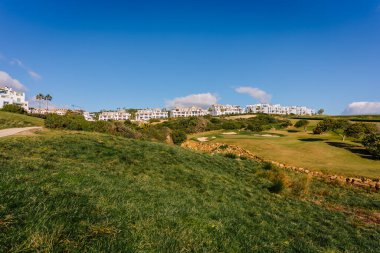 Endülüs, İspanya, 30 Ocak 2025 - Yeşil çimenli La Hacienda golf sahasının manzarası, beyaz modern konut binaları, ve arka planda parlak mavi bir gökyüzü.