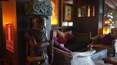 Endülüs, İspanya - 30 Ocak 2025 - Oyma ahşap bir heykel, renkli yastıklar, leopar desenli mobilyalar, fenerler ve yangın söndürücü levhası olan kırsal bir iç mekan.