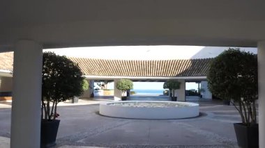 Endülüs, İspanya - 30 Ocak 2025 - Yuvarlak bir çeşmesi, saksı ağaçları ve kiremitli çatı yapıları olan sakin bir avlu, okyanus manzarasına yol açıyor..