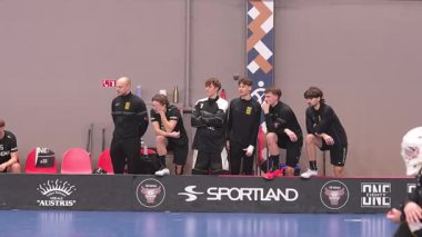Floorball takımının üyeleri ve antrenörleri, siyah üniformalar giyip, spor salonunda maç izlerken dikkatle izliyorlar. Valmiera, Letonya - 5 Şubat 2025 - 