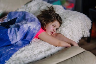 A young child waking up in the morning, lying on a fluffy pillow under a blue blanket, with a sleepy expression, watching TV. clipart