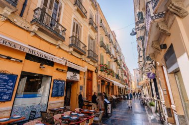 Endülüs, Malaga - 31 Ocak 2025 - Güneşli bir günde renkli binalar, balkonlar, açık kahve masaları ve yayalar ile Malaga 'da büyüleyici dar bir cadde