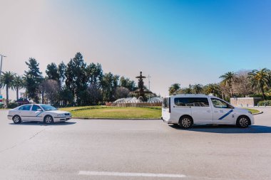 Endülüs, Malaga - 31 Ocak 2025 - Güneşli bir günde ağaçlar, palmiye ağaçları ve yoldan geçen iki taksiyle çevrili bir çeşme.