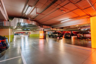 Endülüs, Malaga - 31 Ocak 2025 - Yeraltı otoparkı modern ışıklandırma, park edilmiş arabalar, yansıtıcı yerler, görünür tabelalar ve parlak turuncu bir reklam.