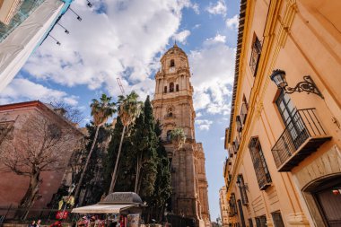 Endülüs, Malaga - 31 Ocak 2025 - Palmiye ağaçları, tarihi binalar ve dağınık şehir merkezli bulutlarla çevrili gökyüzü.