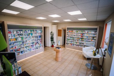 Ilukste, Letonya - 10 Eylül 2024 - Güzellik, vitamin ve sağlık ürünleri sergilenen iyi ışıklandırılmış rafları olan bir eczanenin içi. Küçük bir oturma yeri ve çiçekli bir masa görülebilir..