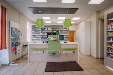 Ilukste, Letonya - 10 Eylül 2024 - Bir tezgahı, ilaç rafları ve sergilenmekte olan, yeşil dekorlu ve organize depolanmış ürünleri olan modern, iyi ışıklandırılmış bir eczane.