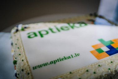 Ilukste, Latvia - September 10, 2024 - Close-up of a decorated cake with a pharmacy logo and website printed on the icing, surrounded by intricate white frosting details. clipart