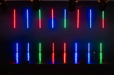 Valmiera, Letonya - 8 Şubat 2025 - Kırmızı, mavi ve yeşil renkli dikey neon ışıklar koyu bir arkaplan üzerinde parlıyor, parlak bir zemin yansıtıyor, canlı bir ekran yaratıyor.