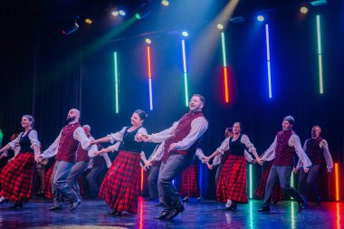 Valmiera, Letonya - 8 Şubat 2025 - 90 'ların partisi. Geleneksel kıyafetli bir grup dansçı renkli ışıklarla aydınlatılmış bir sahnede canlı bir halk dansı yapıyorlar..