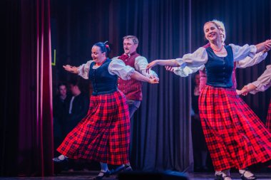 Valmiera, Letonya - 8 Şubat 2025 - 90 'ların partisi. Geleneksel kıyafetli bir grup dansçı renkli ışıklarla aydınlatılmış bir sahnede canlı bir halk dansı yapıyorlar..