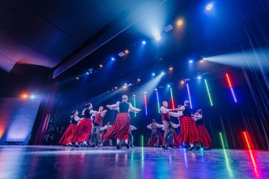 Valmiera, Letonya - 8 Şubat 2025 - 90 'ların partisi. Geleneksel kıyafetli bir grup dansçı renkli ışıklarla aydınlatılmış bir sahnede canlı bir halk dansı yapıyorlar..