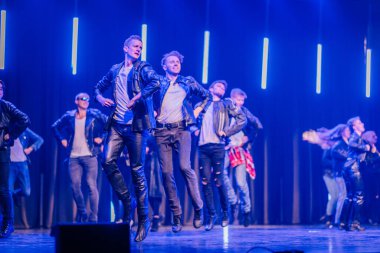 Valmiera, Letonya - 8 Şubat 2025 - 90 'ların partisi. Deri ceketli bir grup dansçıyla sahnede dinamik bir dans gösterisi, enerjik bir sahnede mavi ışıklarla aydınlatılıyor..