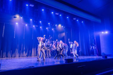 Valmiera, Letonya - 8 Şubat 2025 - 90 'ların partisi. Deri ceketli bir grup dansçıyla sahnede dinamik bir dans gösterisi, enerjik bir sahnede mavi ışıklarla aydınlatılıyor..