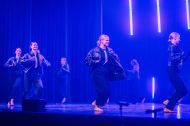 Valmiera, Letonya - 8 Şubat 2025 - 90 'ların partisi. Bir grup siyah elbiseli ve deri ceketli kadın dansçı dramatik ışıklandırmayla sahnede dinamik bir koreografi sergiliyorlar..