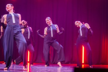 Valmiera, Letonya - 8 Şubat 2025 - 90 'ların partisi. Şık siyah elbiseli ve inci kravatlı bir grup dansçı dramatik kırmızı ışık altında sahnede senkronize bir gösteri sergiliyorlar..