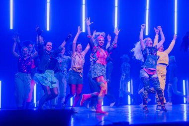 Valmiera, Letonya - 8 Şubat 2025 - 90 'ların partisi. Renkli retro giysiler içinde canlı bir grup kadın neon ışıkları altında enerjik bir şekilde dans ediyor, neşe ve coşku saçıyorlar..