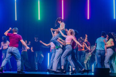 Valmiera, Letonya - 8 Şubat 2025 - 90 'ların partisi. Canlı bir dans gösterisi. Bir grup dansçı, neon ışıklarıyla aydınlatılmış bir sahnede ortağını havaya kaldırıyor..