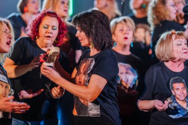 Valmiera, Letonya - 8 Şubat 2025 - 90 'ların partisi. Aynı tişörtleri giyen ve ünlü yüzleri olan kadınlar koro performansında klasik bir telefon tutarak nostaljik bir sahne yaratıyorlar..