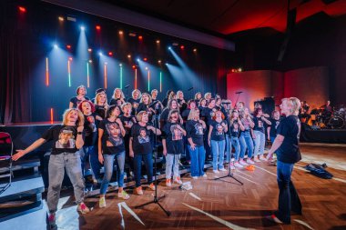 Valmiera, Letonya - 8 Şubat 2025 - 90 'ların partisi. Bir kadın korosu sahnede, duygusal ifadeleri ve senkronize el hareketleriyle uyumlu siyah tişörtler giyerek şarkı söyler.