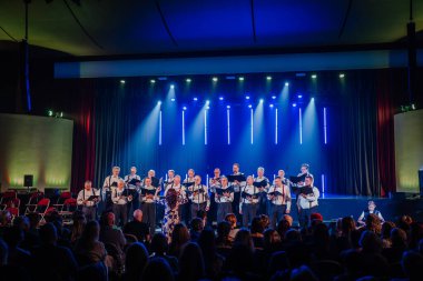 Valmiera, Letonya - 8 Şubat 2025 - 90 'ların partisi. Bir erkek korosu sahneye resmi giysiler içinde, elinde notalarla çıkıyor. Sahne ışıklandırması seyirciler için uyum sağlayan şarkıcıları vurgular..