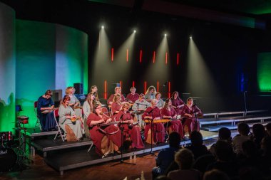 Valmiera, Latvia - February 8, 2025 - 90's party. A womens folk ensemble in Latvian national costumes performs on stage, playing kokles in a traditional music event clipart