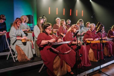 Valmiera, Latvia - February 8, 2025 - 90's party. A womens folk ensemble in Latvian national costumes performs on stage, playing kokles in a traditional music event clipart