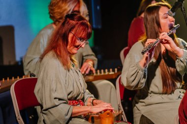 Valmiera, Latvia - February 8, 2025 - 90's party. A womens folk ensemble in Latvian national costumes performs on stage, playing kokles in a traditional music event clipart