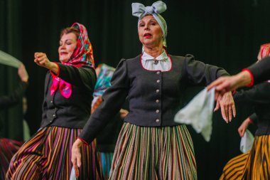 Valmiera, Letonya - 8 Şubat 2025 - 90 'ların partisi. Letonya geleneksel kostümlü bir grup kadın dansçı dramatik ışıklandırma altında beyaz mendillerini sallayarak sahnede halk dansı yapıyorlar..
