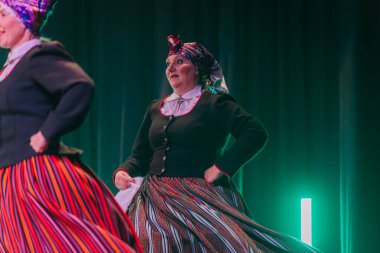 Valmiera, Letonya - 8 Şubat 2025 - 90 'ların partisi. Letonya geleneksel kostümlü bir grup kadın dansçı dramatik ışıklandırma altında beyaz mendillerini sallayarak sahnede halk dansı yapıyorlar..