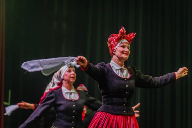 Valmiera, Letonya - 8 Şubat 2025 - 90 'ların partisi. Letonya geleneksel kostümlü bir grup kadın dansçı dramatik ışıklandırma altında beyaz mendillerini sallayarak sahnede halk dansı yapıyorlar..