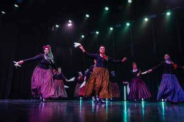 Valmiera, Letonya - 8 Şubat 2025 - 90 'ların partisi. Letonya geleneksel kostümlü bir grup kadın dansçı dramatik ışıklandırma altında beyaz mendillerini sallayarak sahnede halk dansı yapıyorlar..