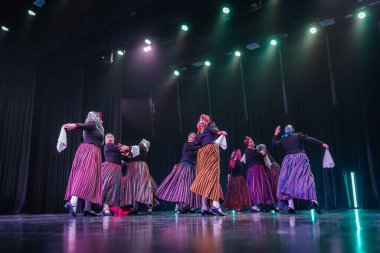 Valmiera, Letonya - 8 Şubat 2025 - 90 'ların partisi. Letonya geleneksel kostümlü bir grup kadın dansçı dramatik ışıklandırma altında beyaz mendillerini sallayarak sahnede halk dansı yapıyorlar..