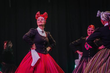 Valmiera, Letonya - 8 Şubat 2025 - 90 'ların partisi. Letonya geleneksel kostümlü bir grup kadın dansçı dramatik ışıklandırma altında beyaz mendillerini sallayarak sahnede halk dansı yapıyorlar..
