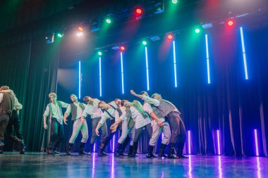 Valmiera, Letonya - 8 Şubat 2025 - 90 'ların partisi. Erkek dansçılar sahnede etkileyici hareketlerle dinamik bir sıçrayış gerçekleştiriyorlar, dramatik ışıklandırma altında eski moda kıyafetler giyiyorlar..