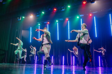 Valmiera, Letonya - 8 Şubat 2025 - 90 'ların partisi. Erkek dansçılar sahnede etkileyici hareketlerle dinamik bir sıçrayış gerçekleştiriyorlar, dramatik ışıklandırma altında eski moda kıyafetler giyiyorlar..