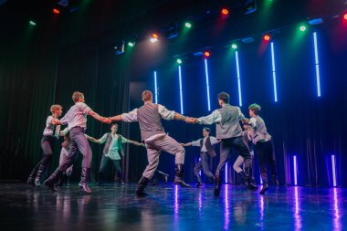 Valmiera, Letonya - 8 Şubat 2025 - 90 'ların partisi. Erkek dansçılar sahnede etkileyici hareketlerle dinamik bir sıçrayış gerçekleştiriyorlar, dramatik ışıklandırma altında eski moda kıyafetler giyiyorlar..