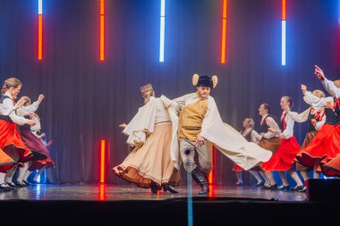 Valmiera, Letonya - 8 Şubat 2025 Letonya 'nın geleneksel halk dansçılarından oluşan bir grup parlak ışıklar altında sahnede enerjik bir gösteri sergiliyor ve 90' ların parti atmosferini canlandırıyor.