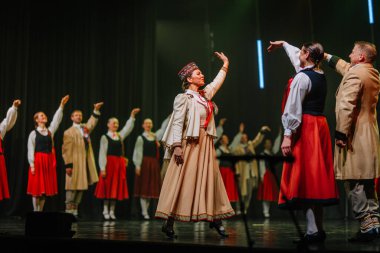 Valmiera, Letonya - 8 Şubat 2025 Letonya 'nın geleneksel halk dansçılarından oluşan bir grup parlak ışıklar altında sahnede enerjik bir gösteri sergiliyor ve 90' ların parti atmosferini canlandırıyor.