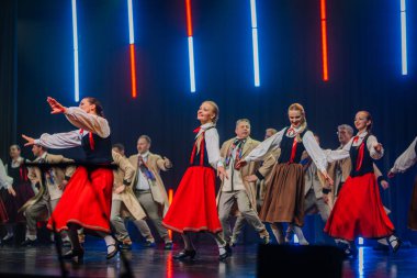 Valmiera, Letonya - 8 Şubat 2025 Letonya 'nın geleneksel halk dansçılarından oluşan bir grup parlak ışıklar altında sahnede enerjik bir gösteri sergiliyor ve 90' ların parti atmosferini canlandırıyor.