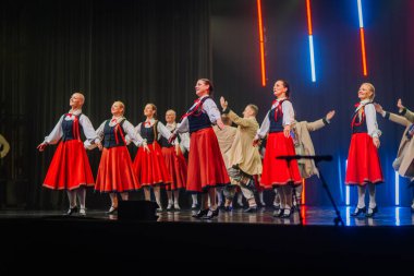 Valmiera, Letonya - 8 Şubat 2025 Letonya 'nın geleneksel halk dansçılarından oluşan bir grup parlak ışıklar altında sahnede enerjik bir gösteri sergiliyor ve 90' ların parti atmosferini canlandırıyor.