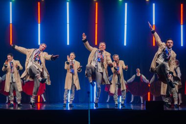 Valmiera, Letonya - 8 Şubat 2025 Letonya 'nın geleneksel halk dansçılarından oluşan bir grup parlak ışıklar altında sahnede enerjik bir gösteri sergiliyor ve 90' ların parti atmosferini canlandırıyor.