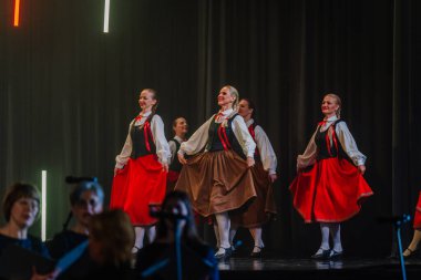 Valmiera, Letonya - 8 Şubat 2025 - Geleneksel folklor kostümlü bir grup kadın dansçı, parlak ışıklar altında sahnede performans sergiliyor.