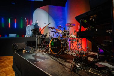 Valmiera, Latvia - February 8, 2025 - A music stage setup featuring a drum kit, keyboard, guitar, and microphones with colorful stage lighting in the background. clipart